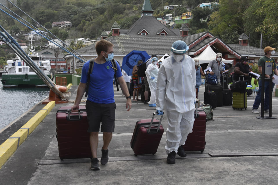 A healthcare worker helps an evacuee with his luggage as British, Canadian and U.S. nationals wait to board the Royal Caribbean cruise ship Reflection, in Kingstown, on the eastern Caribbean island of St. Vincent, Friday, April 16, 2021. La Soufriere volcano has shot out another explosive burst of gas and ash Friday morning as the cruise ship arrived to evacuate some of the foreigners who had been stuck on a St. Vincent island by a week of violent eruptions. (AP Photo/Orvil Samuel)