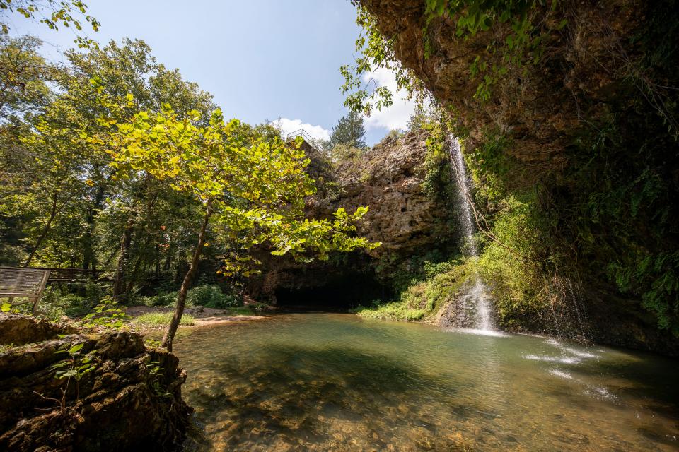 Natural Falls State Park features a 77-foot waterfall cascading through rock formations and creating a hidden, serene atmosphere at the bottom of a narrow V-shape valley.