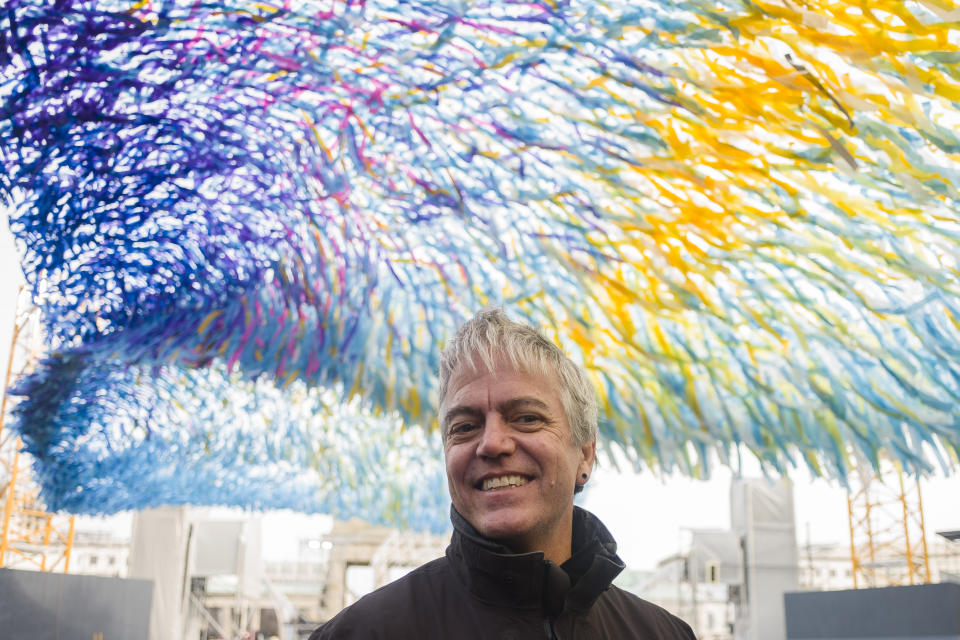 Artist Patrick Shearn poses for media in under his skynet artwork 'Visions In Motion' at the 'Strasse des 17. Juni' (Street of June 17) boulevard in front of the Brandenburg Gate in Berlin, Germany, Friday, Nov. 1, 2019. Shearn's artwork was made with about 100.000 streamers with written messages and is part of the celebrations marking the 30th anniversary of the fall of the Berlin Wall on Nov 9, 2019. (AP Photo/Markus Schreiber)