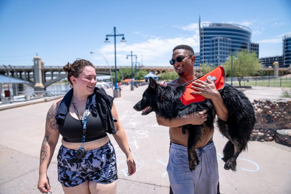 Alex Ramirez, left, walks with her boyfriend Josh Hempstead as he carries their long-haired German shepherd Noctis so she does not burn her paws on the sidewalk after paddle boarding at Tempe Town Lake on July 13, 2023.