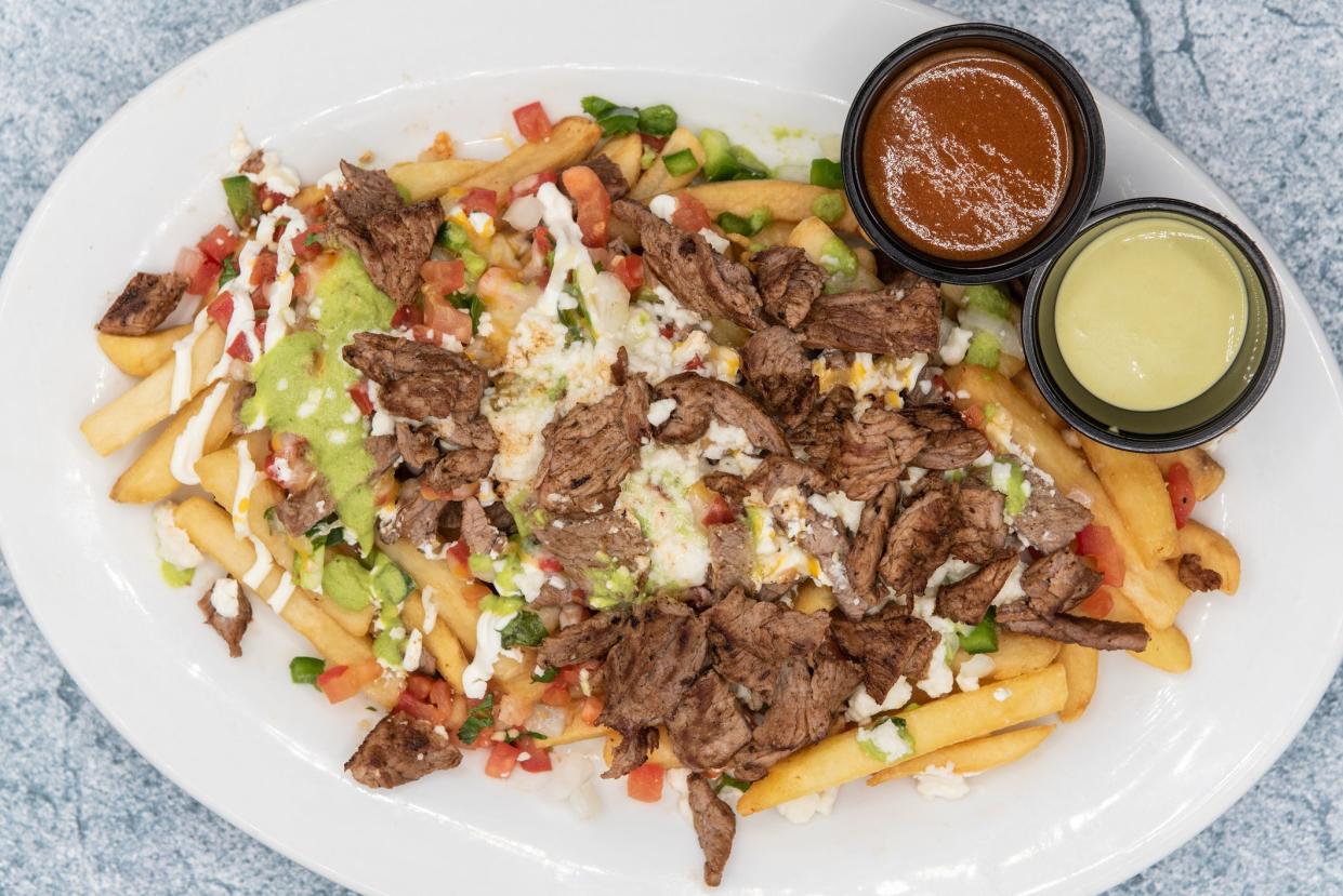 Overhead view of large plate of Asada french fries covered in cheese served with dipping sauce will tempt everyone.