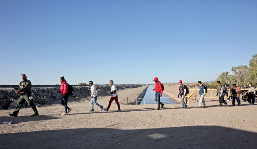 A border patrol agent leads asylum seekers to a van for transport along the Mexico/USA border, next to Cocopah Reservation land in Somerton, Arizona, on Thursday, May 4, 2023. Immigrants cross the border unimpeded and wait at this location for border patrol officers to take them to the Yuma Customs and Border Protection processing center.