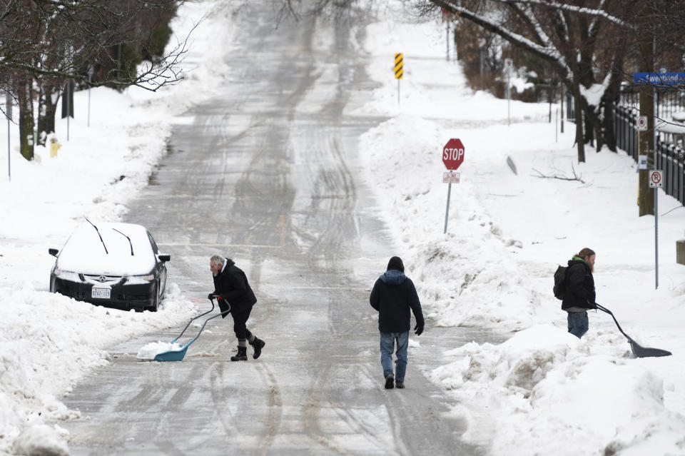 People shovel snow in the Sandy Hill neighborhood of Ottawa, on Friday, Dec. 23, 2022. Environment Canada has issued a winter storm warning for the region which is calling for flash freezing, icy and slippery surfaces, wind gusts and chills. (Spencer Colby /The Canadian Press via AP)