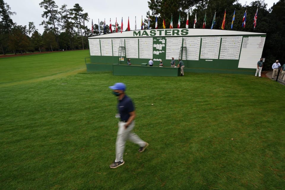 A man wearing a face mask during the coronavirus outbreak walks past the scoreboard during the first round of the Masters golf tournament Friday, Nov. 13, 2020, in Augusta, Ga. (AP Photo/Matt Slocum)