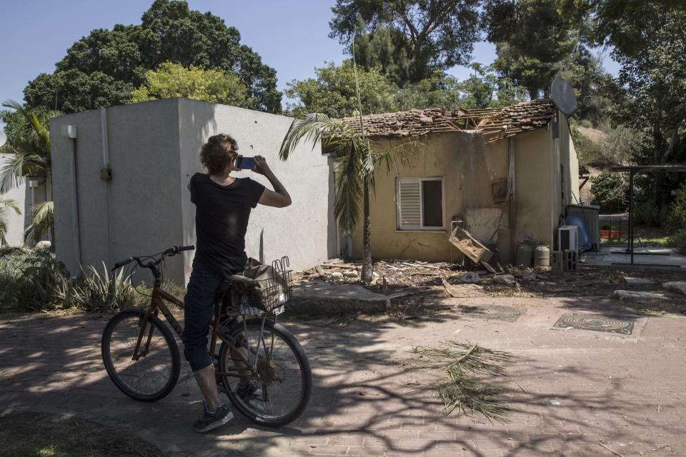 A woman takes a photo of a house damaged by a missile fired from Gaza Strip, in a kibbutz near the Israel and Gaza border, Thursday, Aug. 9, 2018. Israeli warplanes struck dozens of targets in the Gaza Strip and three people were reported killed there, while Palestinian militants from the territory fired scores of rockets into Israel in a fierce burst of violence overnight and into Thursday morning. (AP Photo/Tsafrir Abayov)