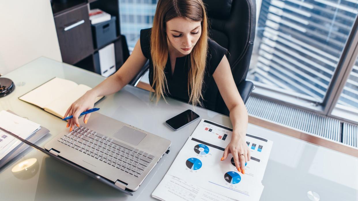 Female businesswoman readind financial report analyzing statistics pointing at pie chart working at her desk.