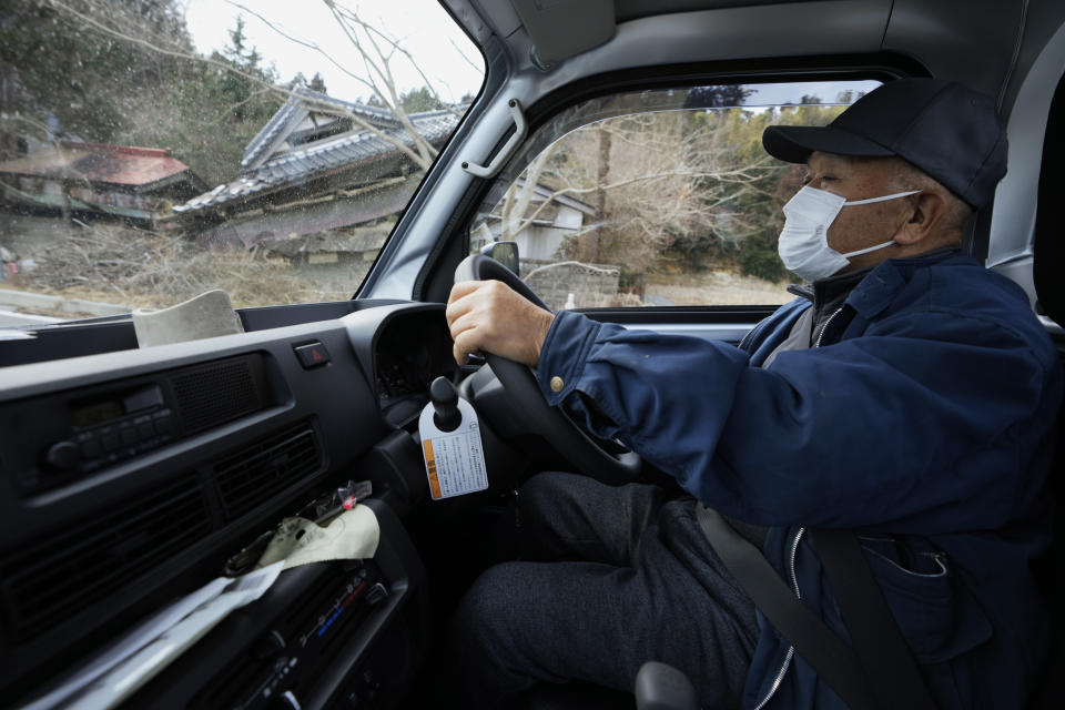 Yasushi Hosozawa drives past damaged buildings in Futaba town, northeastern Japan, Wednesday, March 2, 2022, on his way back from buying his lunch in Namie town. He often drives to Namie, a neighboring town, for his favorite meals. Hosozawa returned his home in Futaba 11 years after he evacuated following the 2011 earthquake, which caused a nuclear crisis in the area. (AP Photo/Hiro Komae)