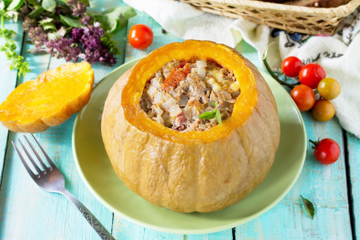 Meatloaf-stuffed mini pumpkin on a green plate with a fork, mini tomatoes, and herbs on a light blue table