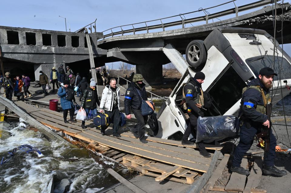 Ukrainian police officers help residents to cross a destroyed bridge as they evacuate Irpin, northwest of Kyiv, on March 12, 2022. - Russian forces stepped up the pressure on Kyiv on March 12, 2022. The northwest suburbs of the capital, including Irpin and Bucha, have already endured days of heavy bombardment while Russian armoured vehicles are advancing on the northeastern edge. (Photo by Sergei SUPINSKY / AFP) (Photo by SERGEI SUPINSKY/AFP via Getty Images)