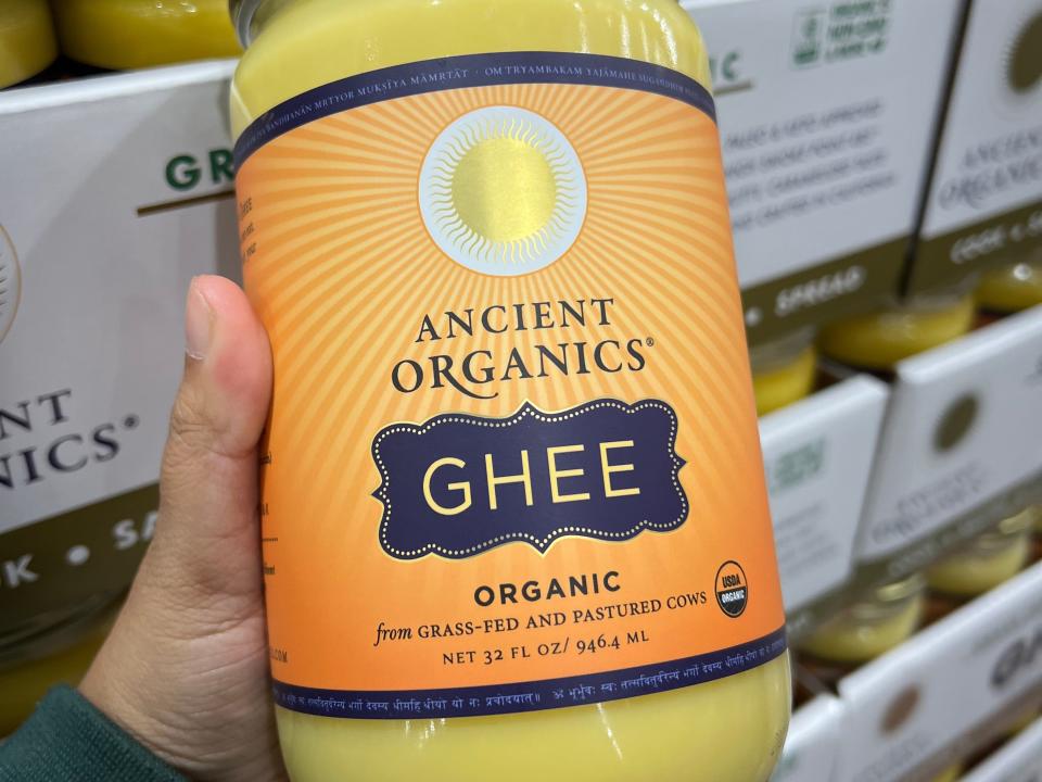 A hand holding a jar of Ancient Organics organic Ghee.