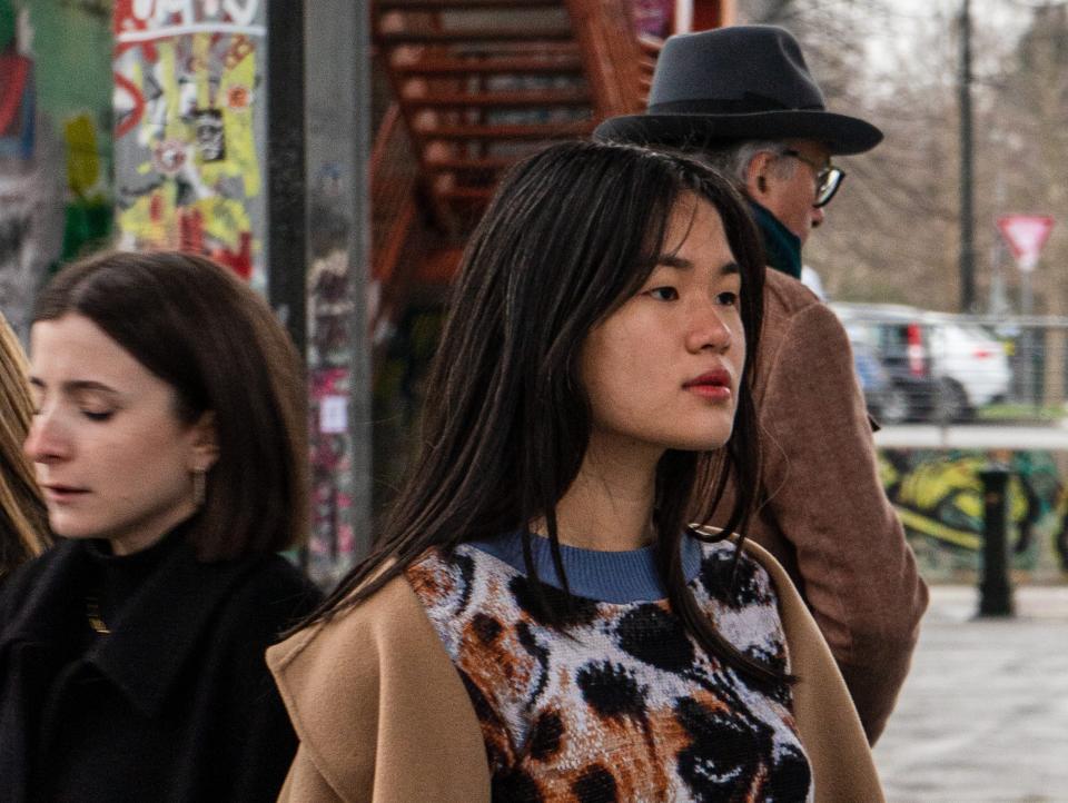 A woman walks through city streets wearing one of Cap_able's knitted garments under a brown jacket