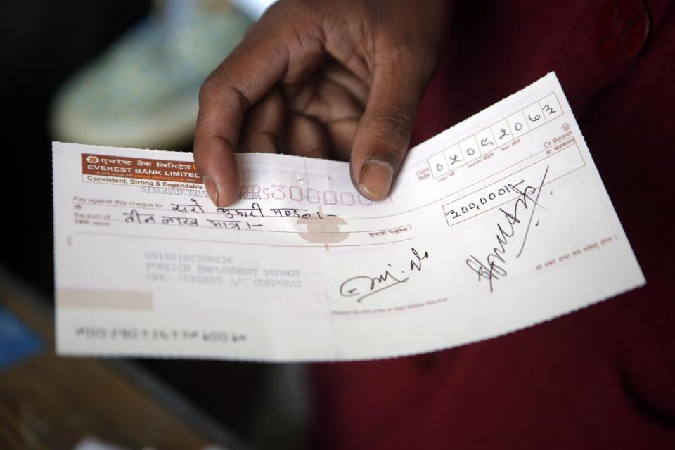 In this Tuesday, Dec 20, 2016 photo, Saro Kumari Mandal, 26, holds a cheque received as compensation from the Foreign Employment Promotion Board after her husband died as a migrant worker in Qatar, in Kathmandu, Nepal. She received $2,777 which she said she would use to open a small store in the village selling cookies and noodles, and also invest in a sewing machine. She wants to earn money for their son's education. "I want to make my son a teacher or a doctor when he grows up," she said. (AP Photo/Niranjan Shrestha)