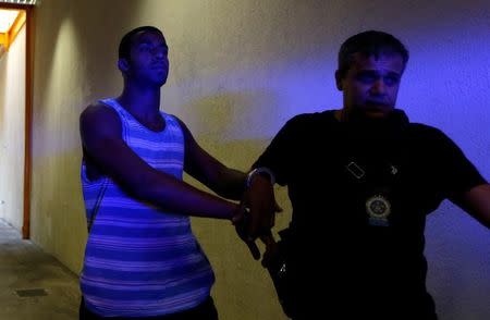 Rai de Souza (L), 22, suspected of being involved in the gang rape of a teenage girl, with a video of the assault circulated widely on social media, is escorted at the Police Station for crimes against minors in Rio de Janeiro, Brazil, May 30, 2016. REUTERS/Ricardo Moraes