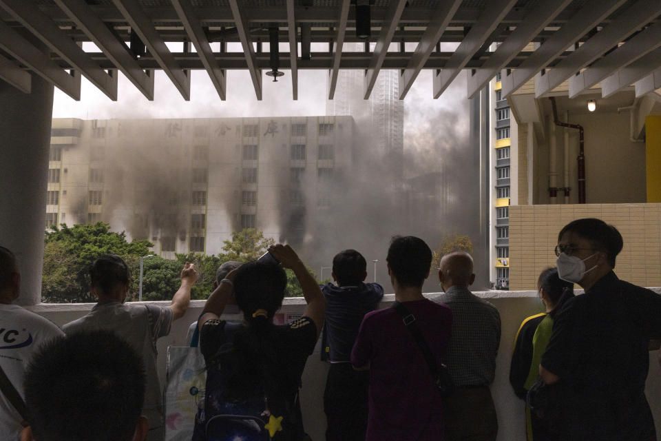 Passerby watch a fire from a footbridge in Cheung Sha Wan, a residential and industrial area, in Hong Kong, Friday, March 24, 2023. (AP Photo/Louise Delmotte)