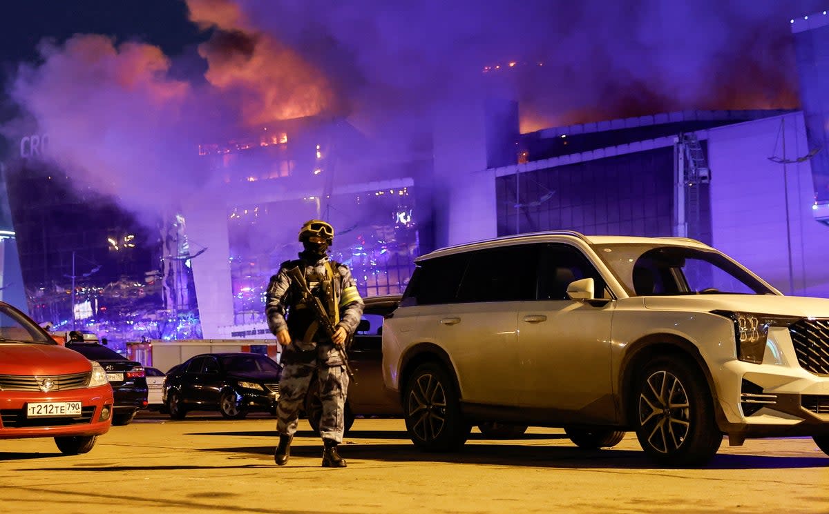 A Russian law enforcement officer walks at a parking area near the burning Crocus City Hall concert venue following a shooting incident, outside Moscow, Russia, 22 March 2024 (REUTERS)