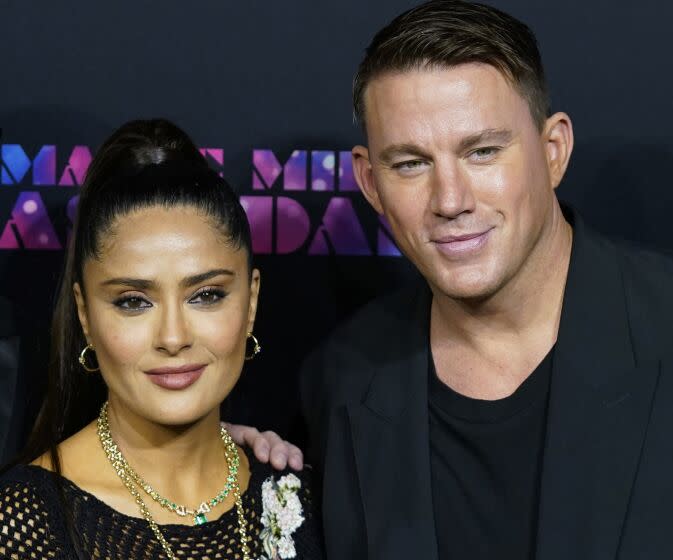 A woman, left, poses for photographers while a taller man stands to the right, posing with a hand on her shoulder