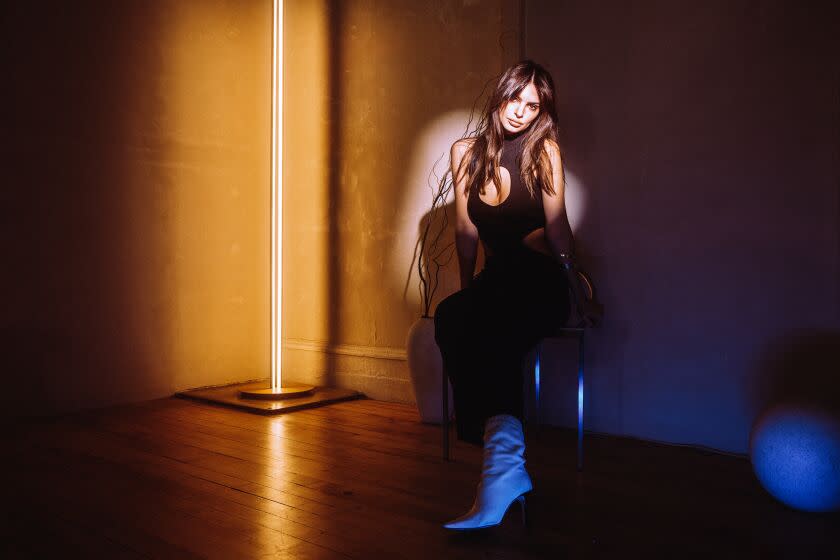 A woman sits on a chair in a dark room, her face in spotlight