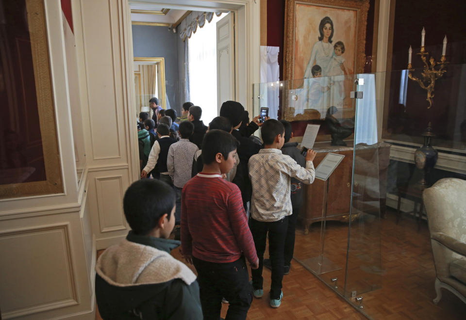 In this Tuesday, Jan. 15, 2019 photo, a group of Iranian schoolboys visit Niavaran Palace, now a museum, that was the primary and last residence of late Shah Mohammad Reza Pahlavi and his family prior to leaving Iran for exile during the 1979 Islamic Revolution, in northern Tehran, Iran. The palace complex of mansions on a 27-acre plot, nestled against the Alborz Mountains, now welcomes the public to marvel at the luxuries the shah enjoyed as Iran's monarch for nearly four decades. It costs about $1 to enter. The painting at right shows then Empress Farah Pahlavi and two of her children. (AP Photo/Vahid Salemi)