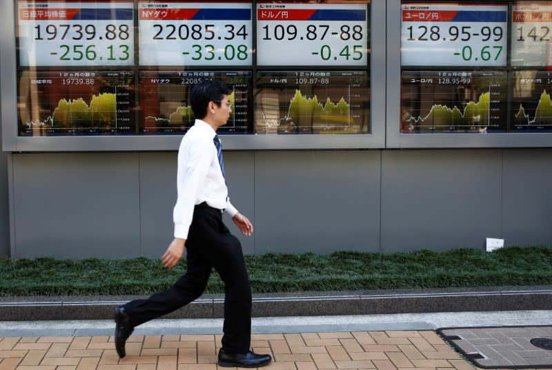 FILE PHOTO - A man walks past electronic boards showing Japan's Nikkei average (L), the Dow Jones Industrial Average (2nd L) and foreign exchange rates outside a brokerage at a business district in Tokyo, Japan August 9, 2017. REUTERS/Kim Kyung-Hoon