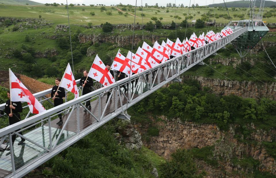 people walking and carrying the Georgian flag over a glass bridge above Dashbashi Canyon in the country of Georgia