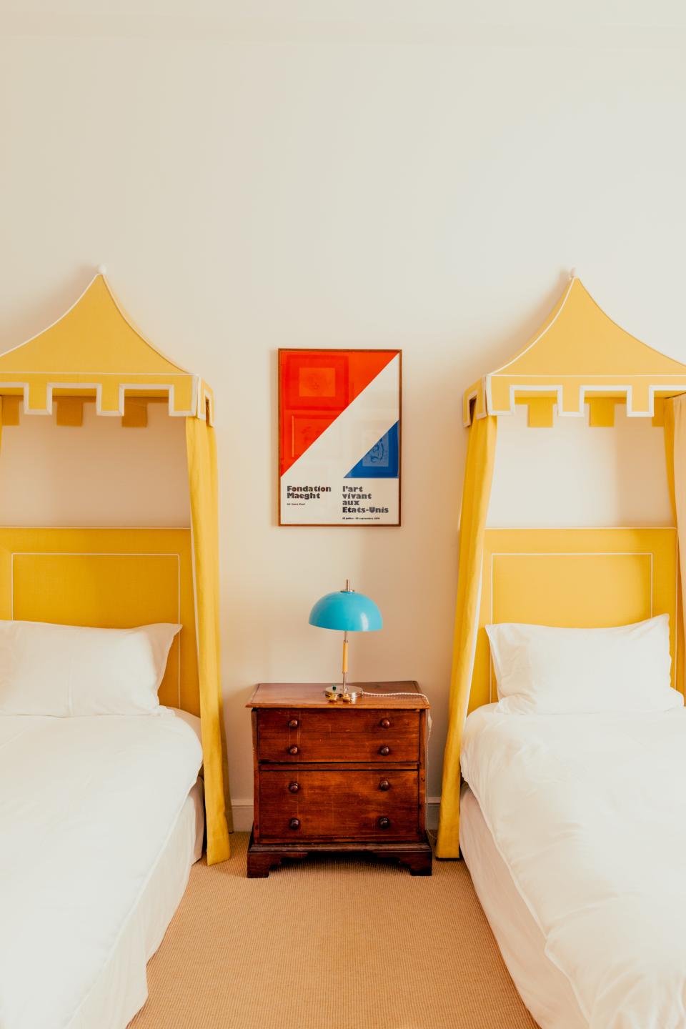 In the children's bedroom, the custom headboards and canopies are made of a Pierre Frey fabric. A 1950s table lamp sits atop a 19th-century English side table.