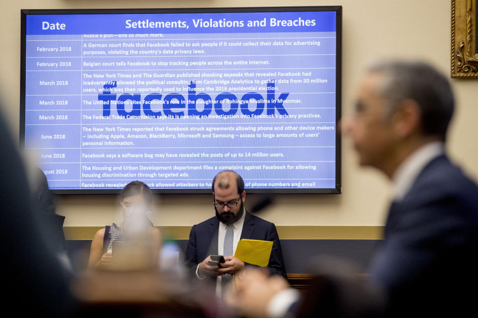 A list of settlements, violations and breaches scrolls over Facebook's logo on a screen as David Marcus, CEO of Facebook's Calibra digital wallet service, foreground, appears before a House Financial Services Committee hearing on Facebook's proposed cryptocurrency on Capitol Hill in Washington, Wednesday, July 17, 2019. (AP Photo/Andrew Harnik)