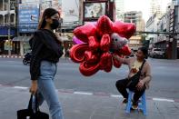 A woman wearing protective walks past a woman selling ballons to celebrate Valentine's Day in Bangkok