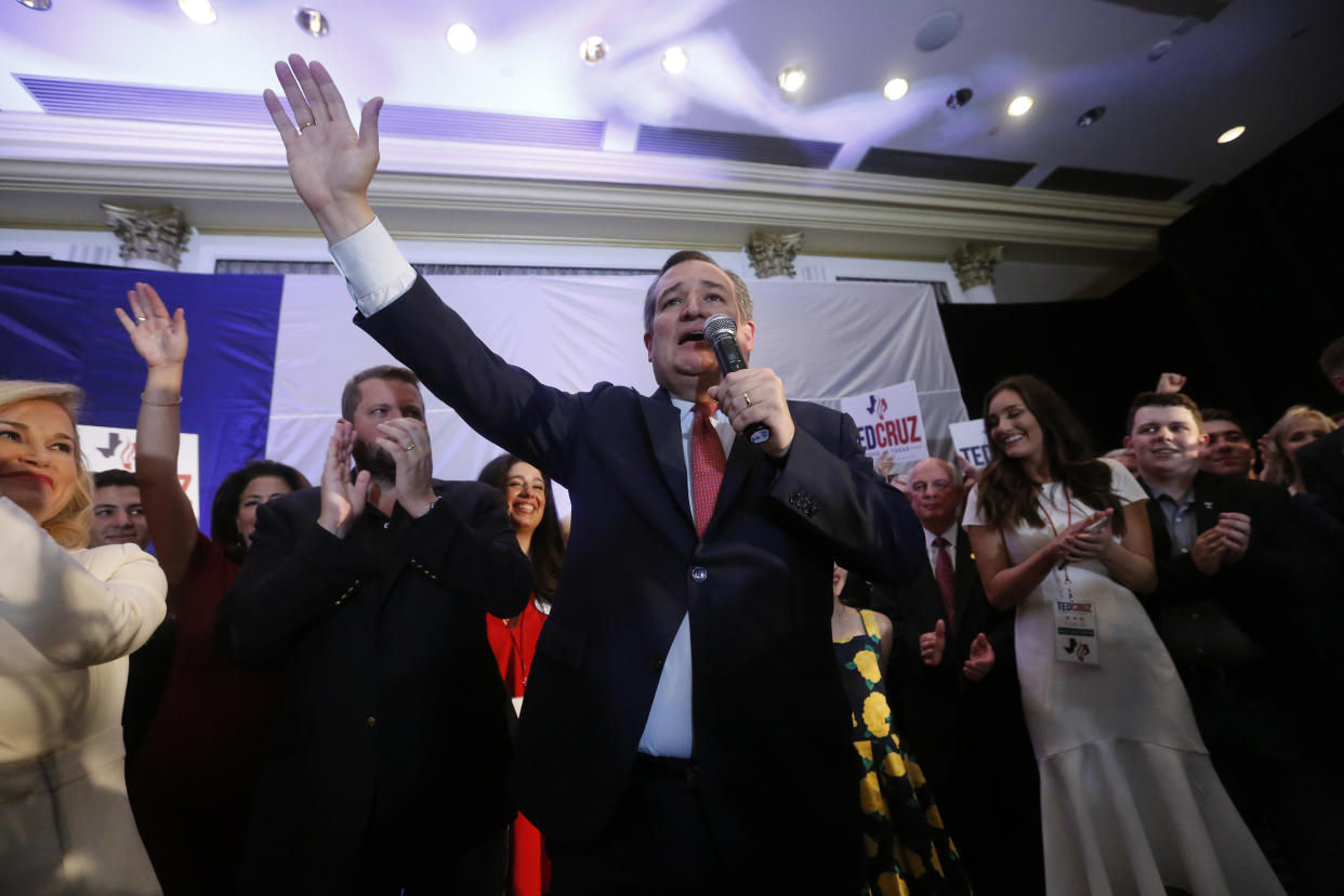 Sen. Ted Cruz raises one hand, a microphone in the other, as well-wishers applaud behind him.