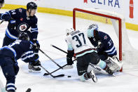 Seattle Kraken Yanni Gourde (37) tries to gain control of the puck in front of Winnipeg Jets goaltender Connor Hellebuyck (37) during the third period of an NHL hockey game in Winnipeg, Manitoba on Tuesday April 16, 2024. (Fred Greenslade/The Canadian Press via AP)