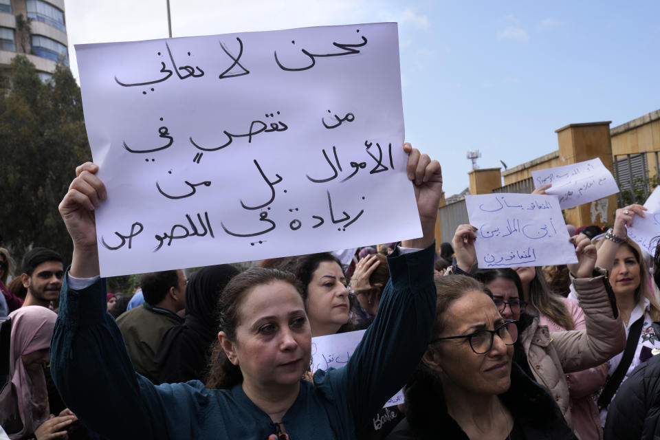 A teacher holds up an Arabic placard that reads: "We don't suffer from a money shortage, but increase in thieves," during a protest outside the Education Ministry in Beirut, Lebanon, Monday, March 6, 2023. Lebanon's education system is in crisis. Public schools have been open for fewer than 50 days this school year because teachers are on strike, protesting dramatic currency devaluations that slashed their salaries to about $20 a month. (AP Photo/Hussein Malla)