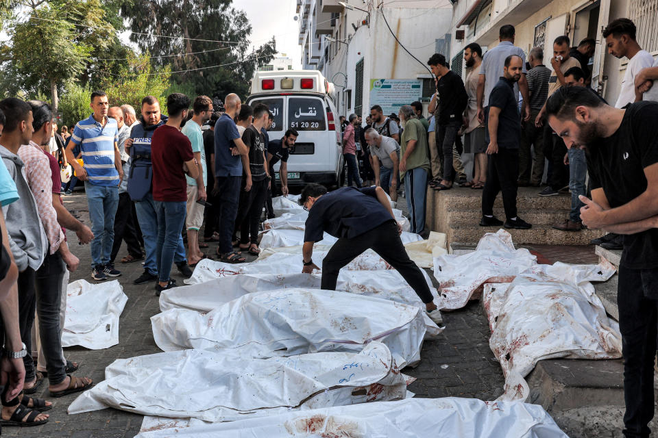 People stand by the bodies of victims of Israeli air strikes outside the morgue of Al-Shifa Hospital in Gaza City, 