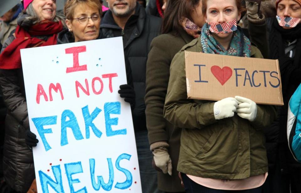 Protesters hold placards saying 'I am not fake news' and 'I love facts'