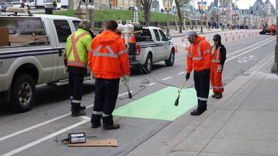 Workers paint a bike lane green on Wellington Street in downtown Ottawa April 27, 2023, the day before this part of the road reopens to public vehicles.