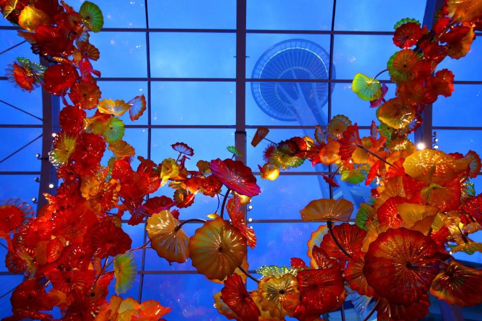 In this May 16, 2012 photo, the Space Needle towers over the Glasshouse at the new Dale Chihuly Garden and Glass museum at the Seattle Center. Fifty years after the World's Fair inserted the Space Needle into Seattle's skyline, the city is celebrating that anniversary by offering an array of new things to see and do at Seattle Center: from a zip line to the new art glass museum.(AP Photo/seattlepi.com, Joshua Trujillo) MAGS OUT; NO SALES; SEATTLE TIMES OUT; MANDATORY CREDIT; TV OUT