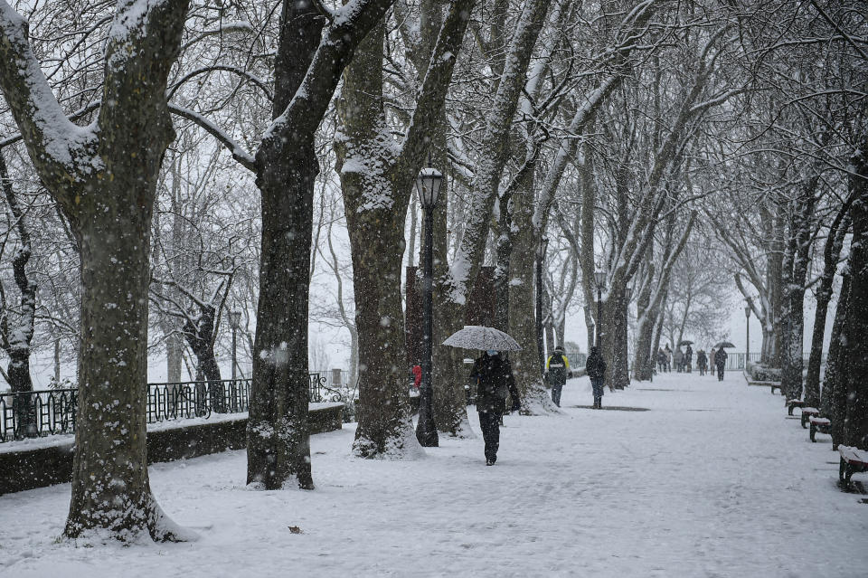 Gente caminando con paraguas por un paseo bajo la nieve en Pamplona, en el norte de España, el sábado 9 de enero de 2021. Una inusual y persistente ventisca cubrió de nieve gran parte de España. paralizando el tráfico y dejando a miles de personas atrapadas en autos, estaciones o aeropuertos. (AP Foto/Álvaro Barrientos)