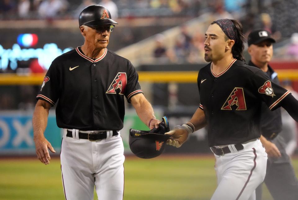 Arizona Diamondbacks first base coach Dave McKay hands a helmet back to baserunner Corbin Carroll (7) as they play against the Milwaukee Brewers at Chase Field in Phoenix on April 12, 2023.