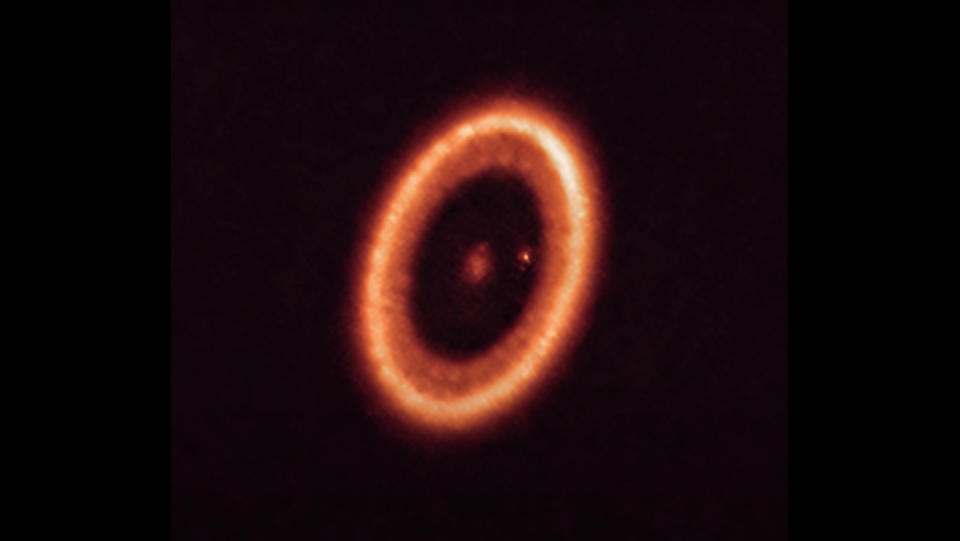 A telescopic image of a planet surrounded by ring of dust and gas, as well as a moon that itself is surrounded by its own ring of dust and gas.