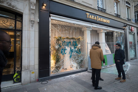 People stand in front of a damaged Tara Jarmon shop during a demonstration by the "yellow vests" movement on the Champs Elysees avenue in Paris, France, March 16, 2019. Picture taken March 16, 2019. REUTERS/Philippe Wojazer