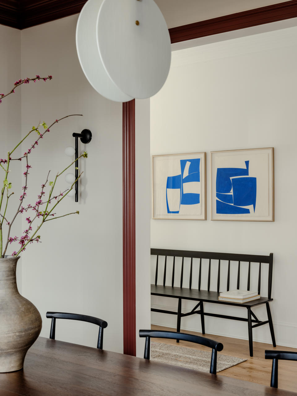 hallway with white walls, blue abstract art and black bench, view through dining room