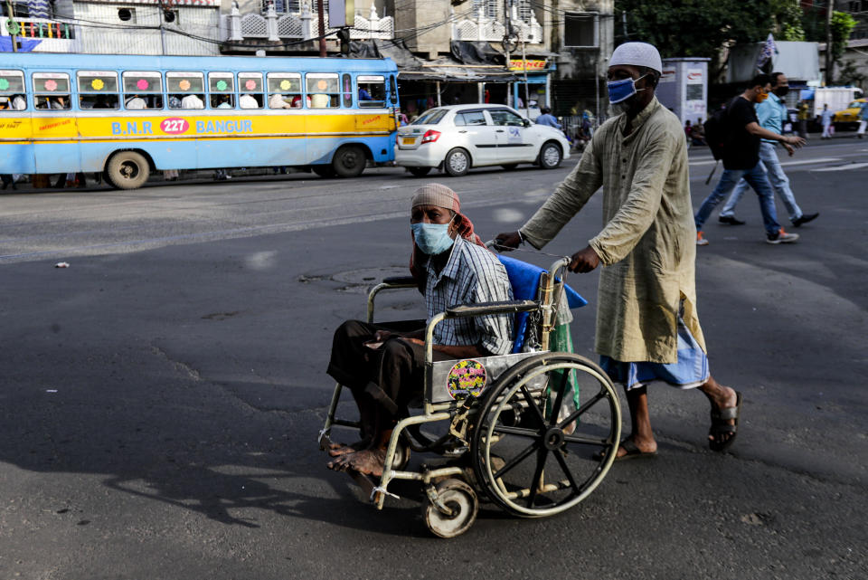 A man pushes a disabled man on wheelchair, both wearing face masks to prevent spreading coronavirus in Kolkata, India, Monday, Oct. 5, 2020. India, the second worst-affected nation in the world after the United States, is witnessing a sustained decline in new coronavirus infections and active virus cases have remained below the million mark for 14 consecutive days. (AP Photo/Bikas Das)