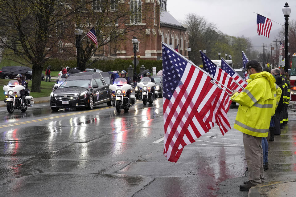 A hearse carrying the coffin of the late U.S. Capitol Police officer William "Billy" Evans, left, drives past people holding flags while escorted by motorcycles though Adams, Mass., following a funeral Mass for Evans, Thursday, April 15, 2021. Evans, a member of the U.S. Capitol Police, was killed on Friday, April 2, when a driver slammed his car into a checkpoint he was guarding at the Capitol. (AP Photo/Steven Senne)