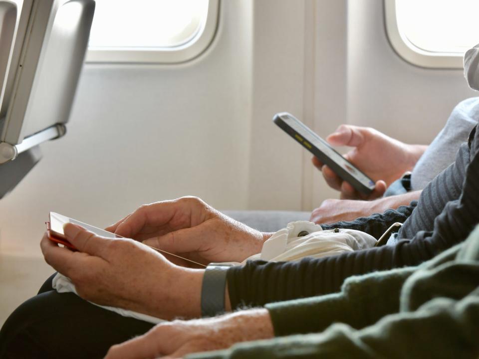 People on an airplane look down at their phones.