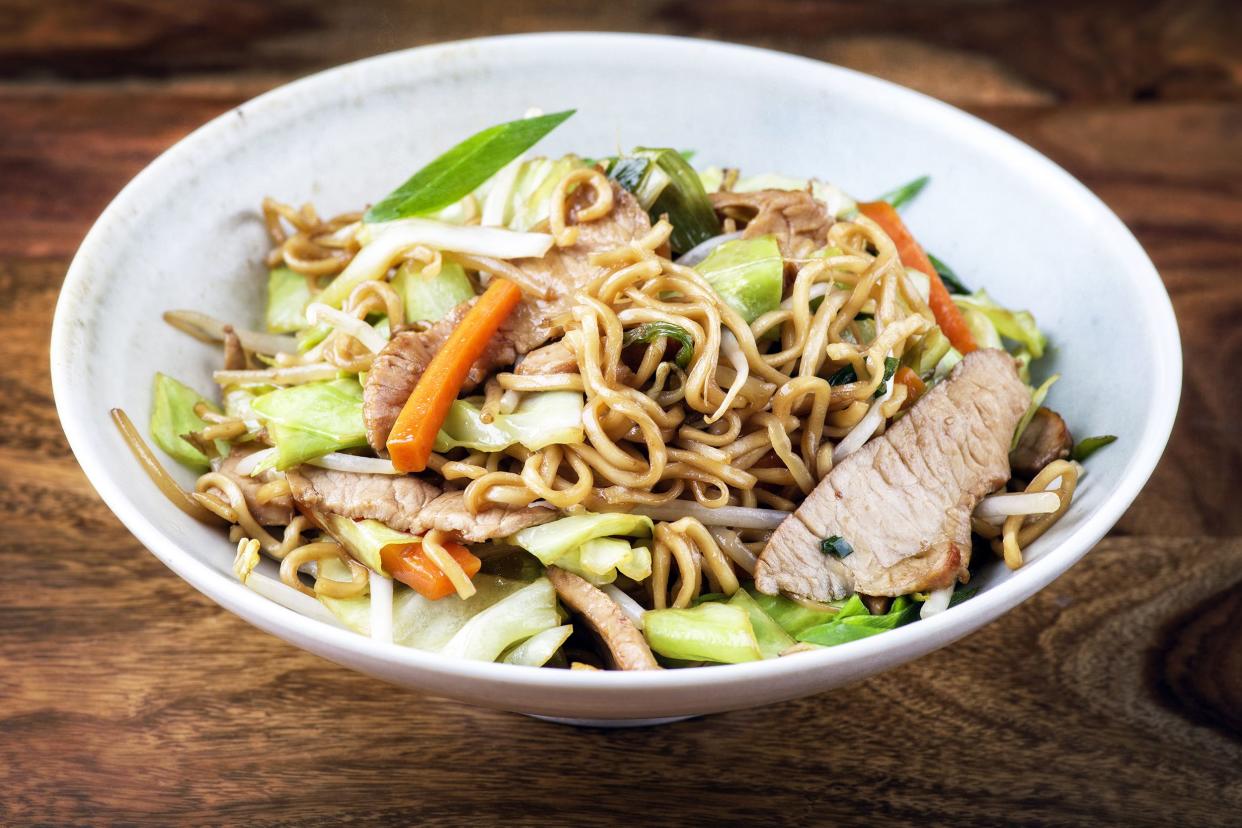 Pork and vegetable lo mein in a white ceramic bowl on a wooden table