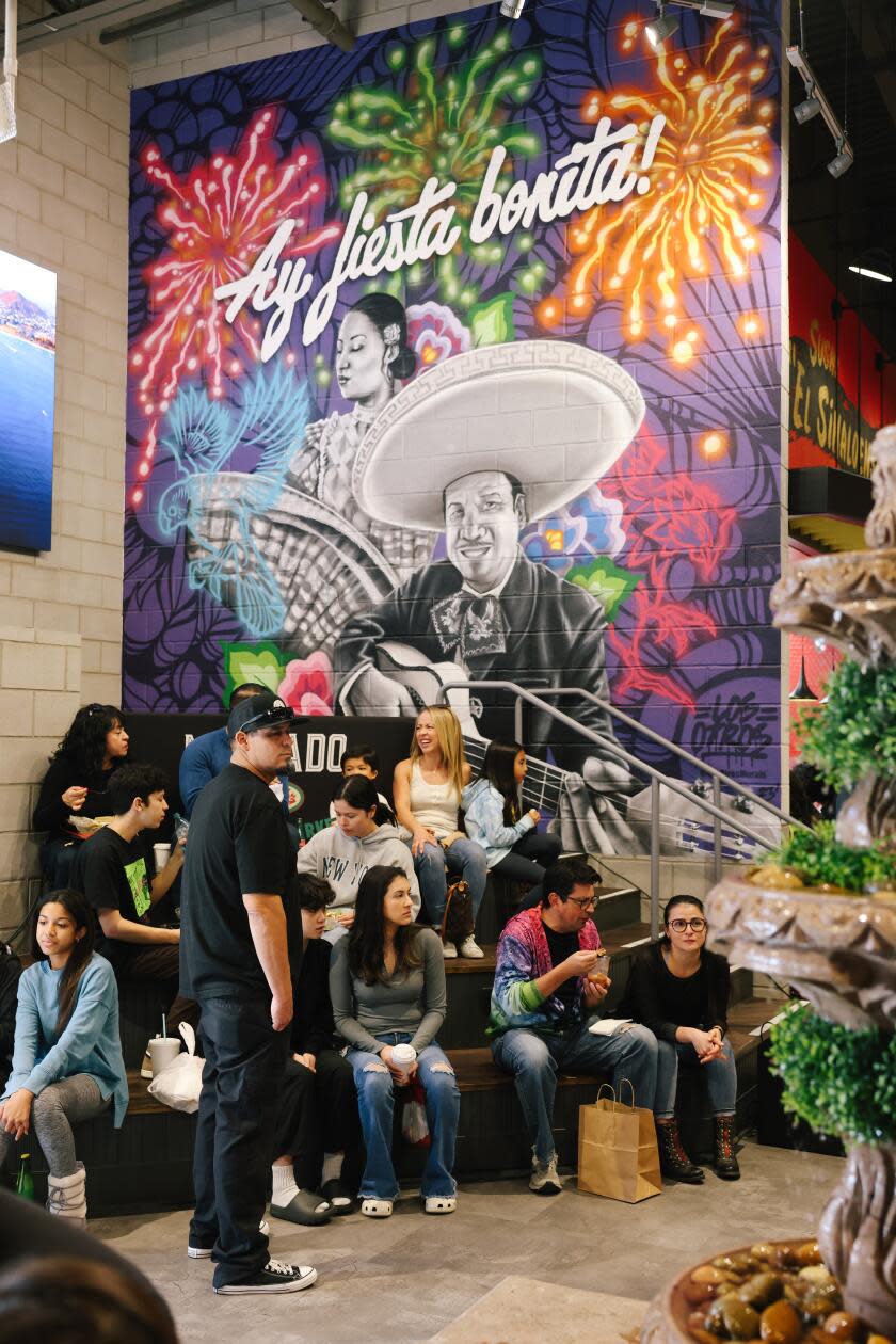 A group of people sitting in front of a colorful indoor mural that reads 