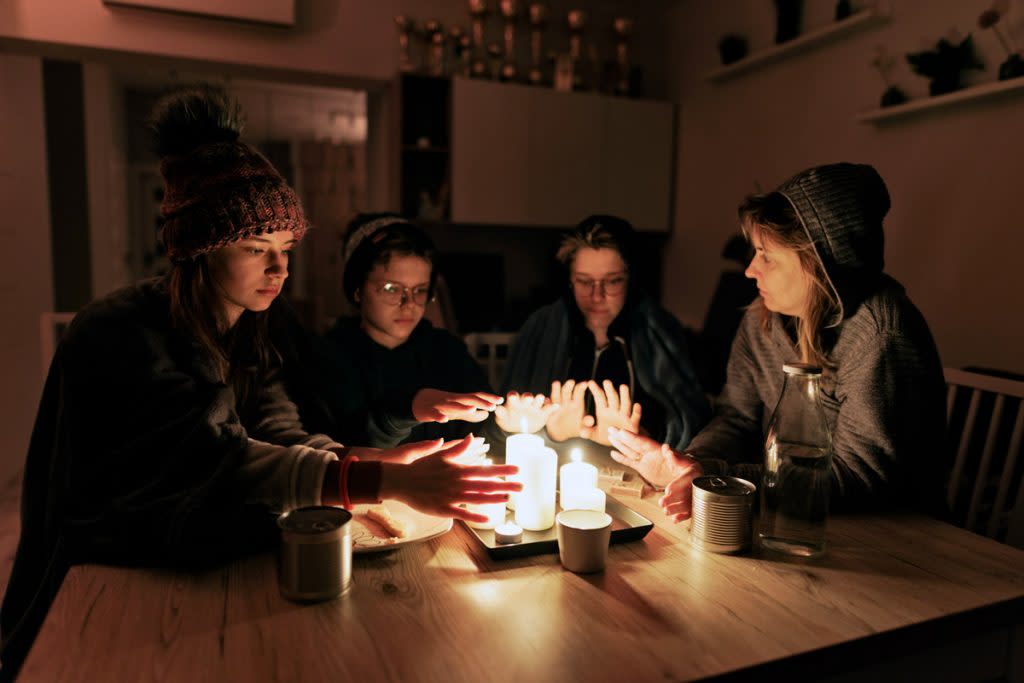 A family wrap themselves in warm clothing and try to get warm by candlelight during a blackout. 