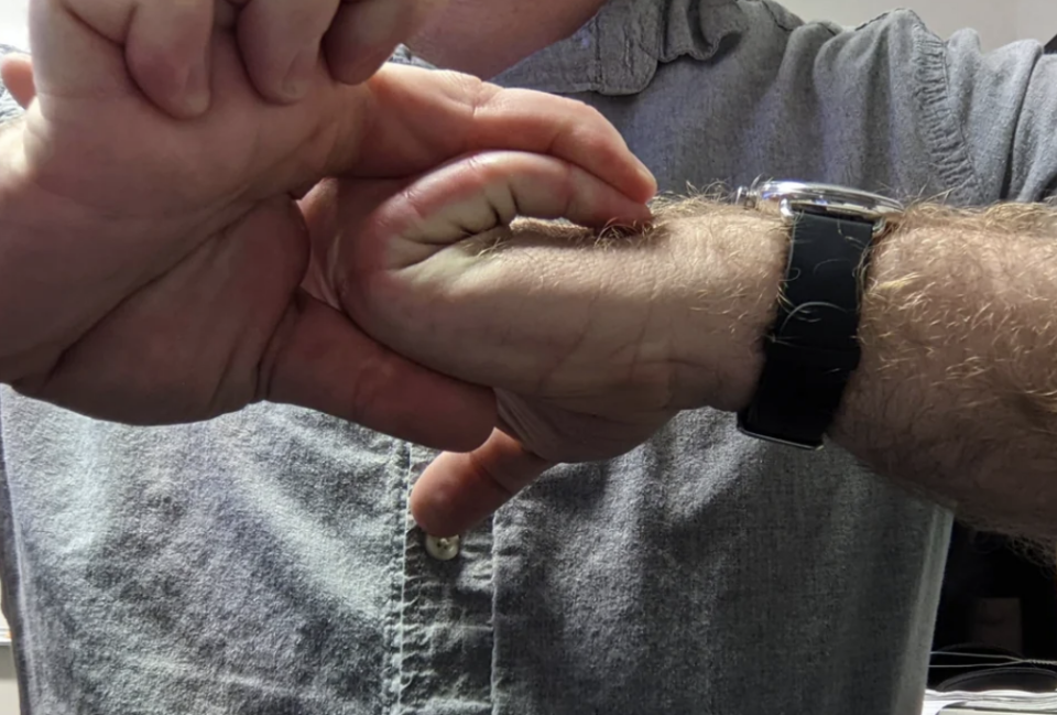 A person demonstrates hand mobility by bending their wrist and fingers back with the other hand. They are wearing a wristwatch and a button-up shirt