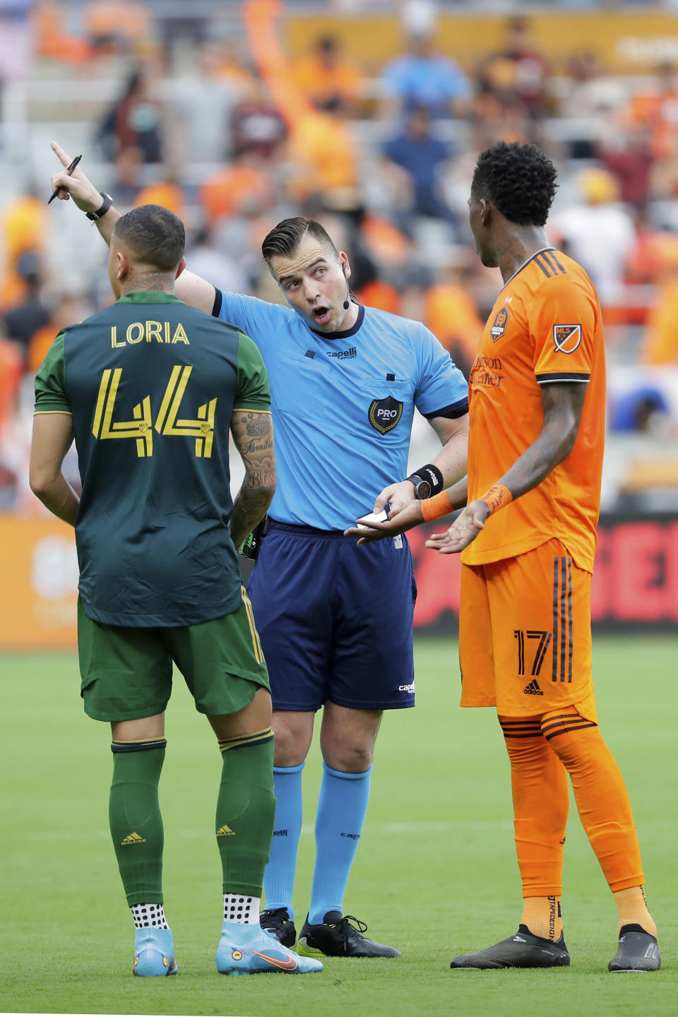 After issuing a red card to Houston Dynamo defender Teenage Hadebe (17), Referee Rosendo Mendoza, center, points off-field telling Hadebe to leave as Portland Timbers midfielder Marvin Loría (44) looks on in during the second half of an MLS soccer match Saturday, April 16, 2022, in Houston. (AP Photo/Michael Wyke)