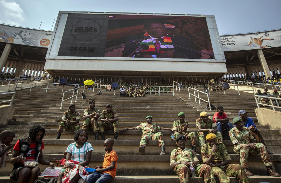 Members of the military sit in the stands as Zimbabwe's President Emmerson Mnangagwa is seen on a video screen above, during the state funeral for former president Robert Mugabe at the National Sports Stadium in the capital Harare, Zimbabwe Saturday, Sept. 14, 2019. African heads of state and envoys gathered to attend a state funeral for Zimbabwe's founding president, Robert Mugabe, whose burial has been delayed for at least a month until a special mausoleum can be built for his remains. (AP Photo/Ben Curtis)