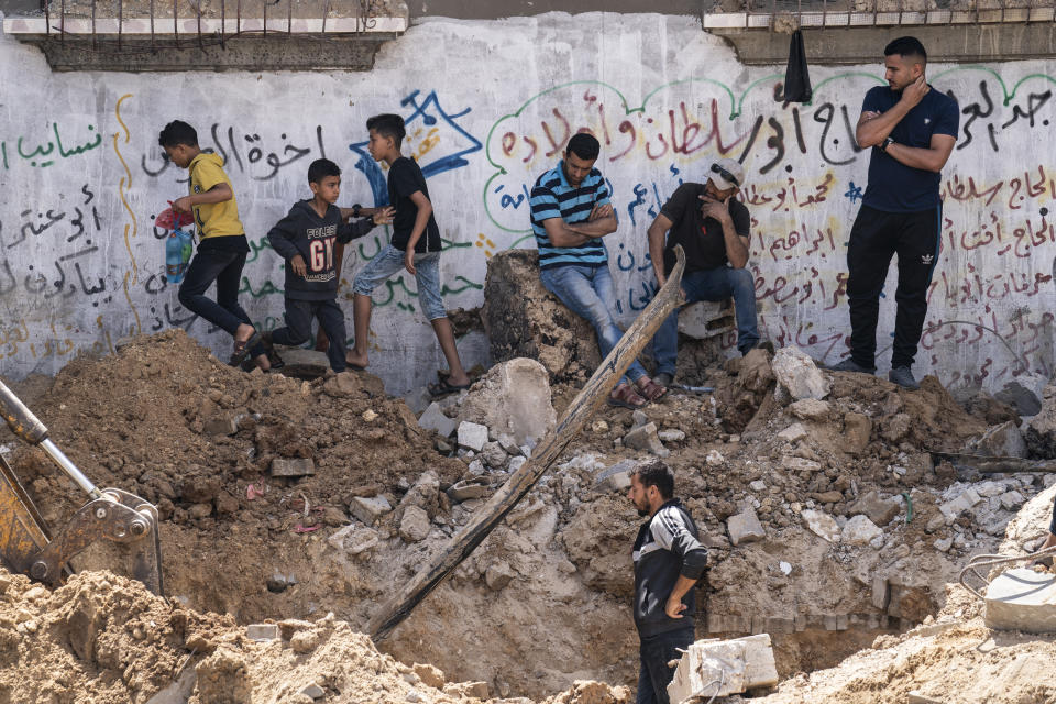 Neighbors gather to watch the cleanup of a crater full of water and sewage after the home of Ramez al-Masri was destroyed by an air-strike prior to a cease-fire reached after an 11-day war between Gaza's Hamas rulers and Israel, Sunday, May 23, 2021, in Beit Hanoun, the northern Gaza Strip. (AP Photo/John Minchillo)