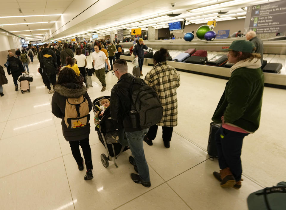 Travelers queue up in baggage claim to wait to pass through the south security checkpoint in Denver International Airport after a winter storm swept over the country packing snow combined with Arctic cold, which created chaos for people trying to reach their destinations before the Christmas holiday, Friday, Dec. 23, 2022, in Denver. Forecasters predict that warmer weather will be on tap for the week ahead. (AP Photo/David Zalubowski)